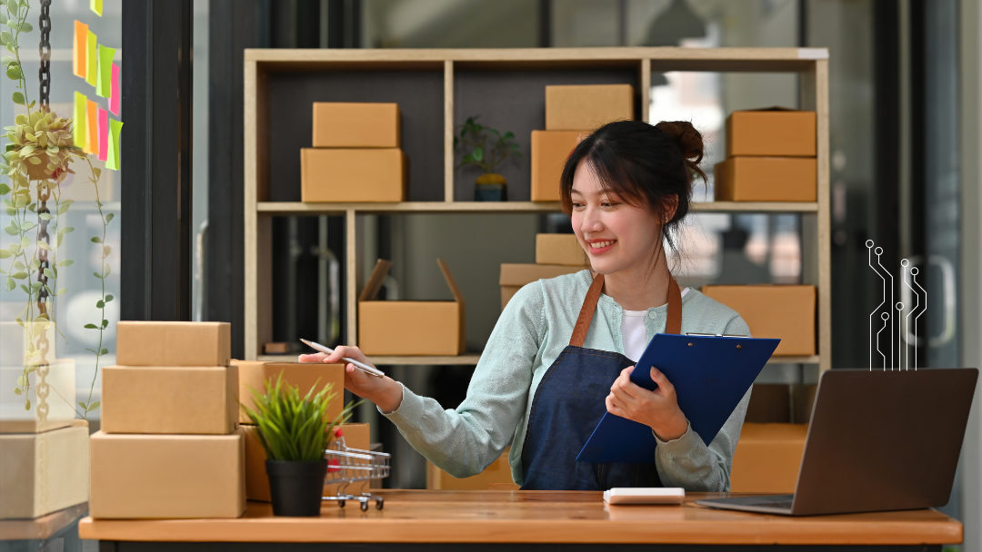 woman stands at her retail counter checking boxes of inventory with an open laptop next to her